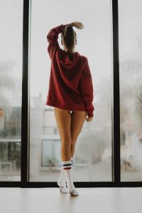 Frau in rotem Pullover steht am Fenster – getragene Unterwäsche anonym verkaufen bei JustOne