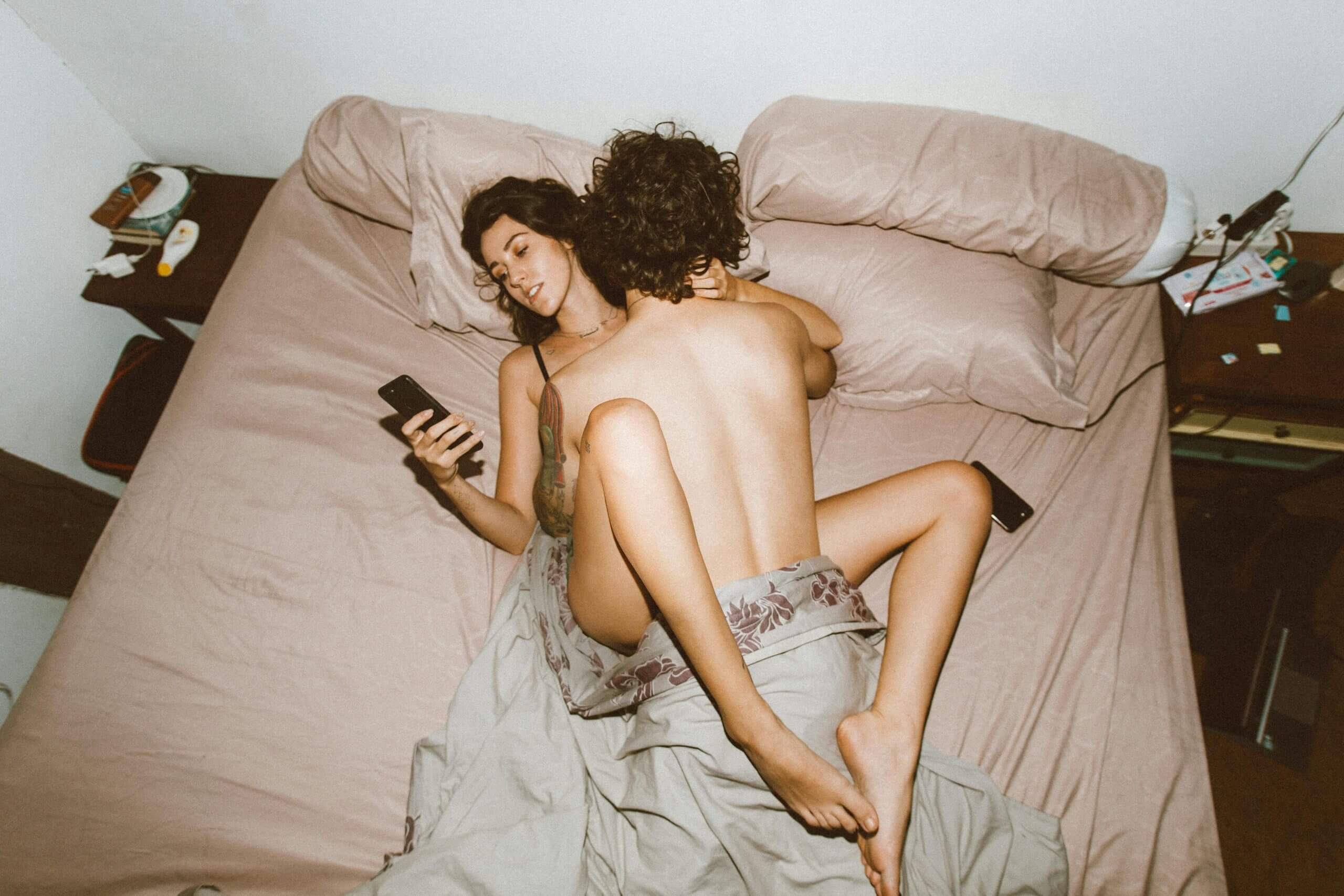 Frau liegt mit Freund im Bett und schaut aufs Handy – anonymer Verkauf von Unterwäsche bei JustOne